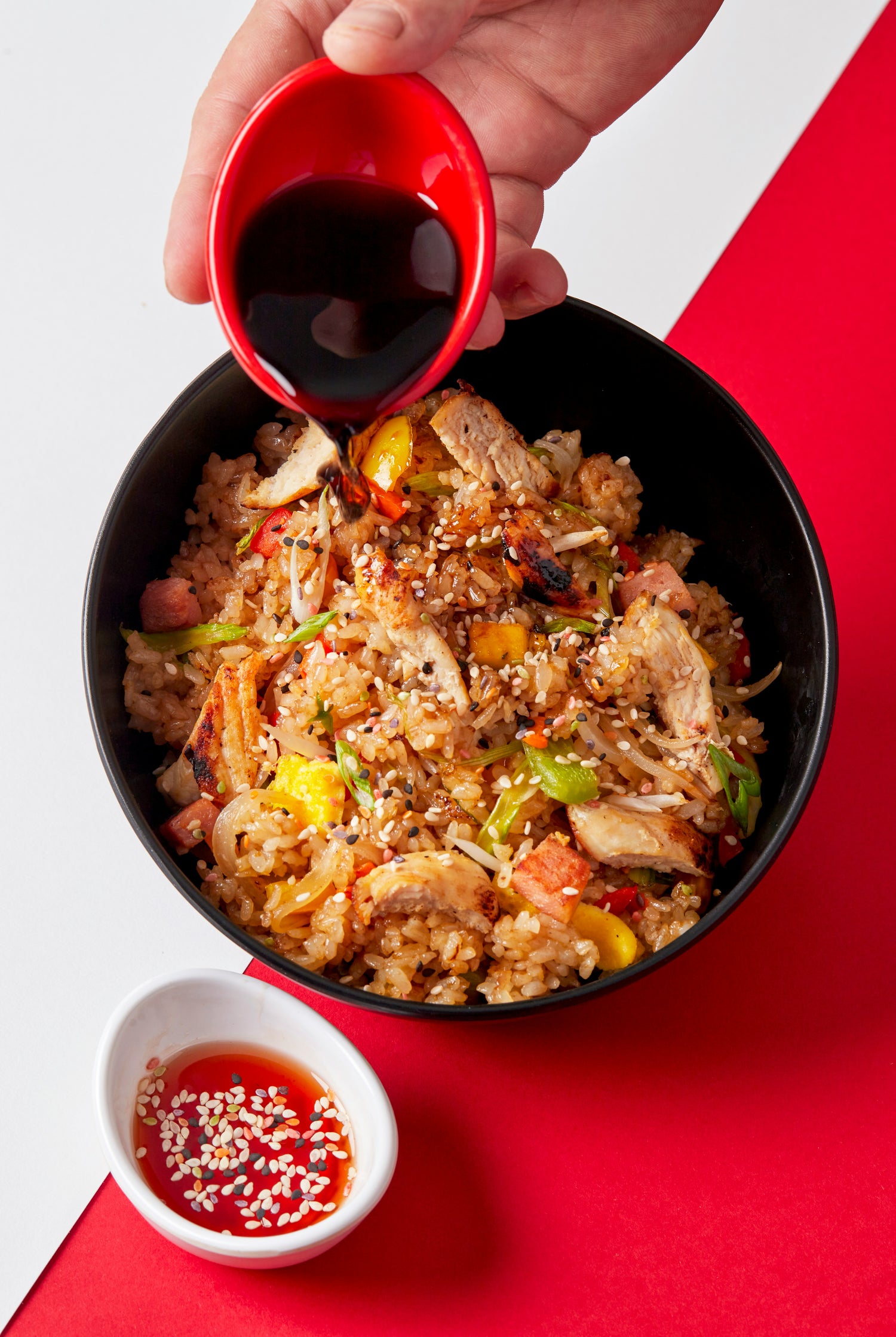 Bratreis mit Hähnchen, Sojasauce wird frisch aufgegossen; dritte Schale mit Sesamöl/Sesamsauce als Beilage.
